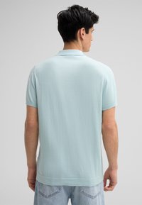 Jasnoniebieska bawełniana koszulka polo z krótkimi rękawami, płaskim kołnierzykiem i prostym dołem. Widok z tyłu ukazuje gładką fakturę i luźny krój.