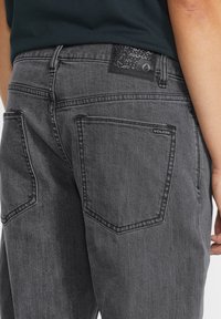Los jeans de mezclilla gris cuentan con un diseño clásico de cinco bolsillos, costuras decorativas y una etiqueta de logo texturizada en negro en la parte trasera de la cinturilla.