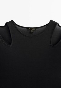 Top smanicato nero a coste con design a spalla scoperta. Realizzato in cotone, presenta un collo arrotondato e una texture sottile. Etichetta visibile.