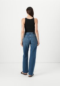 Débardeur noir à côtes associé à un jean en denim bleu taille haute. Présente une coupe droite, deux poches arrière et des coutures minimales.