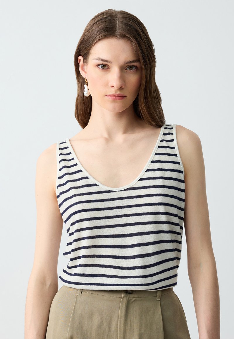 Gestreept tanktop in lichtbeige met navy horizontale strepen, ronde halslijn en dunne schouderbandjes, gecombineerd met beige hoge taille broeken.