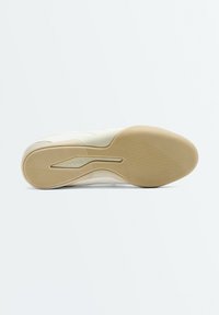 Semelle d'une basket beige avec une bande de roulement en caoutchouc antidérapant et le logo "OYSHO" embossé au niveau du médio-pied.