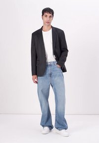 Blazer negro, camiseta blanca, vaqueros de pierna ancha en azul claro y zapatillas blancas. El blazer tiene solapas con muesca y bolsillos discretos.