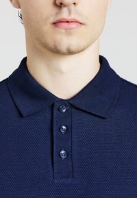 Polo shirt blu navy con tessuto testurizzato, dotato di colletto retrattabile e una chiusura a tre bottoni con bottoni scuri.