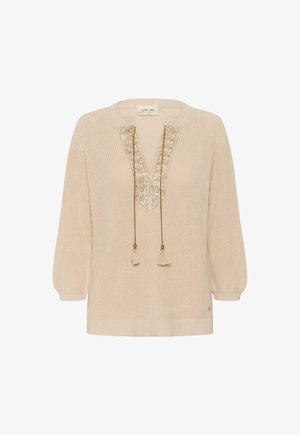 Krēmkrāsas adīta džemperis ar garām piedurknēm, V-veida izgriezums ar zelta izšuvumu apmalē un karājošām pušķu saitēm.