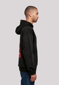 Black hoodie with a red graphic design on the back, featuring a textured fabric, long sleeves, and a drawstring hood.