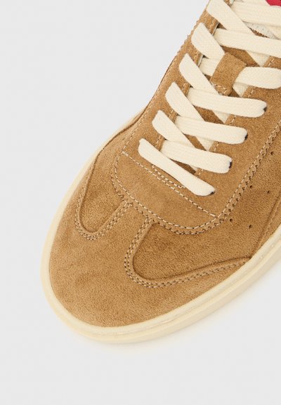 Pantof sport din piele întoarsă maro, cu vârf rotund, șireturi crem și cusături contrastante. Prezintă detalii perforate și o talpă texturată.