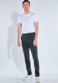 Graue, maßgeschneiderte Hose mit glatter Textur, ausgestattet mit Knopfverschluss und Gürtelschlaufen, kombiniert mit einem schlichten weißen T-Shirt und hellen Sneakern.