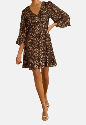 Donna che indossa un vestito marrone al ginocchio con stampa leopardata metallizzata, scollo a V, maniche 3/4 a sbuffo e sandali dorati con tacco alto e cinturini.