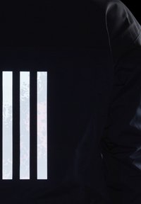 Trois barres blanches verticales avec un motif texturé sur un fond en tissu noir, montrant partiellement une manche côté droit.
