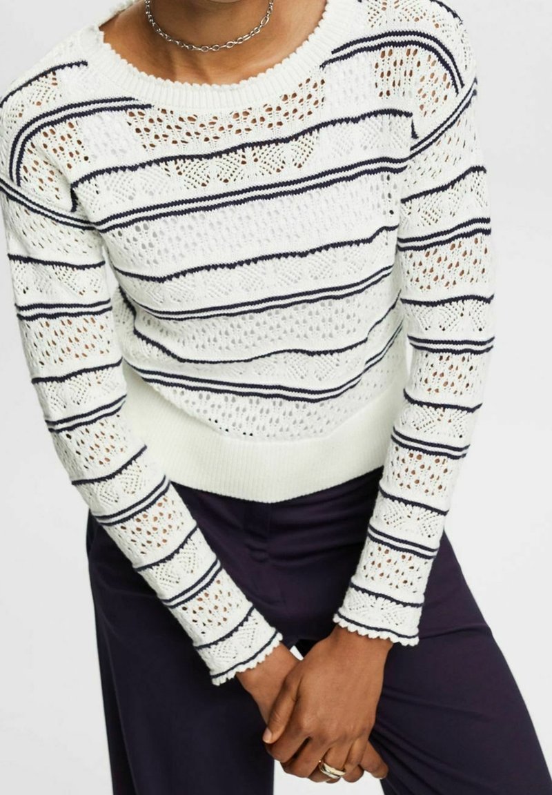 Pull en tricot blanc avec des rayures horizontales bleu marine, présentant un motif texturé et des poignets festonnés. Col rond et coupe ajustée.