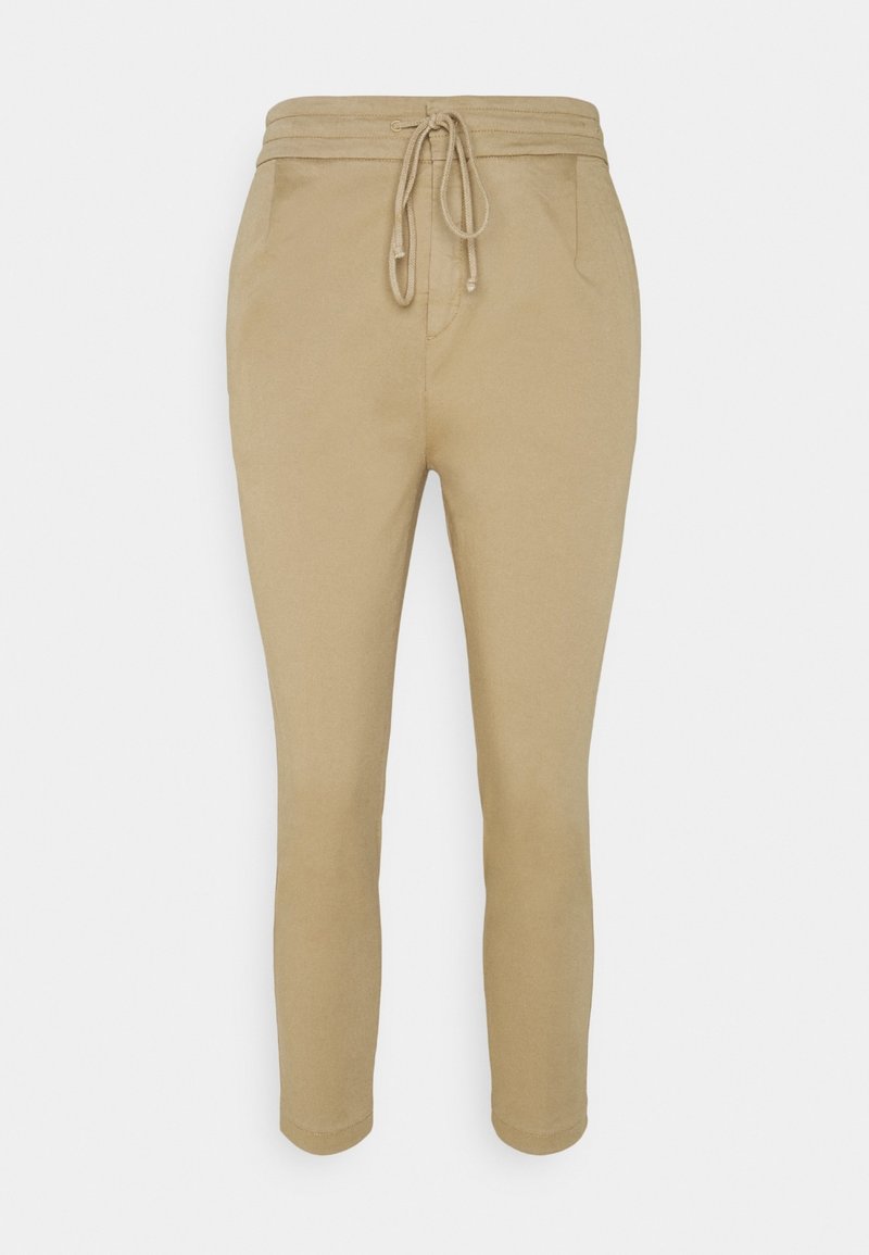 Pantalons tapered beige en tissu doux, avec une taille à cordon et des poches latérales, présentant une texture lisse et un design minimaliste.