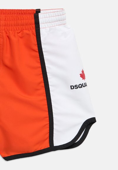 Σύντομα μαγιό με πορτοκαλί και λευκές πάνελ, μαύρο περιθώριο, ελαστική ζώνη και κόκκινο φύλλο σφενδάμου με το κείμενο "DSQUA" στην λευκή πλευρά.