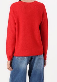 Jersey rojo de punto con textura acanalada, hombros caídos y ajuste holgado. Combinado con vaqueros de mezclilla azul de pierna ancha.