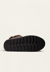 Gummisohle mit einem Zickzackmuster, braunes Kunstfell-Obermaterial und runde Form. Weiche Textur ohne sichtbare Marken oder Akzente.