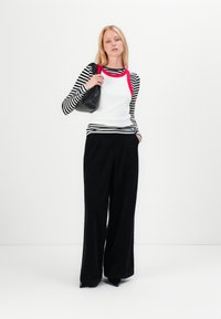 Striped black and white long-sleeve top with red neckline, paired with wide-leg black trousers and a textured black handbag.