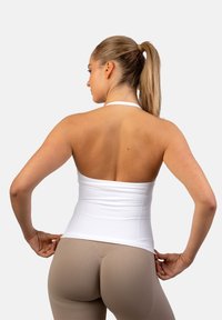 Biały top na ramiączkach o dopasowanym kroju, gładkiej fakturze i bezplecowej stylizacji, zestawiony z beżowymi legginsami, podkreślający smukłą sylwetkę.