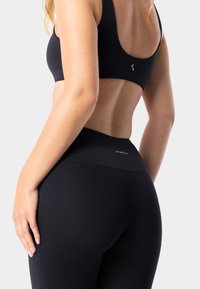 Černá bezšvová sportovní podprsenka a legíny s vysokým pasem. Měkký, elastický materiál s minimálním brandingem, hladká textura a přiléhavý design.