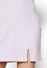 Närbild av en lavendelfärgad och vit rutiga kjol med en liten slits framtill ovanför knäet.