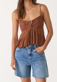 Ruskea, teksturoidulla pinnalla varustettu paita, jossa on pitsikoristeita ja kiristysnyöri, parina vaaleansiniset farkkushortsit, joissa on repsottavat reunat ja sivutaskut.