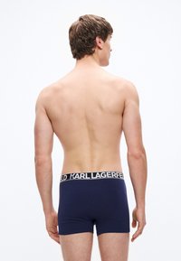 Granatowe bokserki wykonane z miękkiej bawełny, z czarną elastyczną gumką z napisem "KARL LAGERFELD" w białych literach. Gładka tekstura.