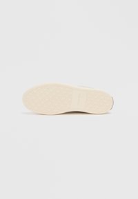 Sole of a light beige sneaker with Calvin Klein logo, featuring a textured pattern of repeated teardrop shapes.