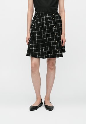Jupe à carreaux noire avec un motif en grille blanche, fabriquée à partir d'un tissu texturé, avec des boutons dorés sur le côté, longueur genou.