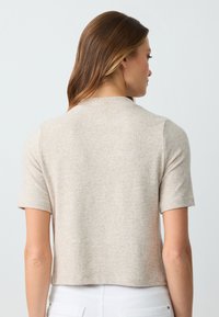 Maglione beige a maniche corte con vestibilità rilassata, motivo a maglia testurizzata e scollatura rotonda, visto da dietro.