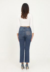 Jeans in denim di lavaggio medio con taglio dritto, caratterizzati da una tasca posteriore a fantasia. Indossati con una maglietta bianca a maniche lunghe e tacchi grigi.