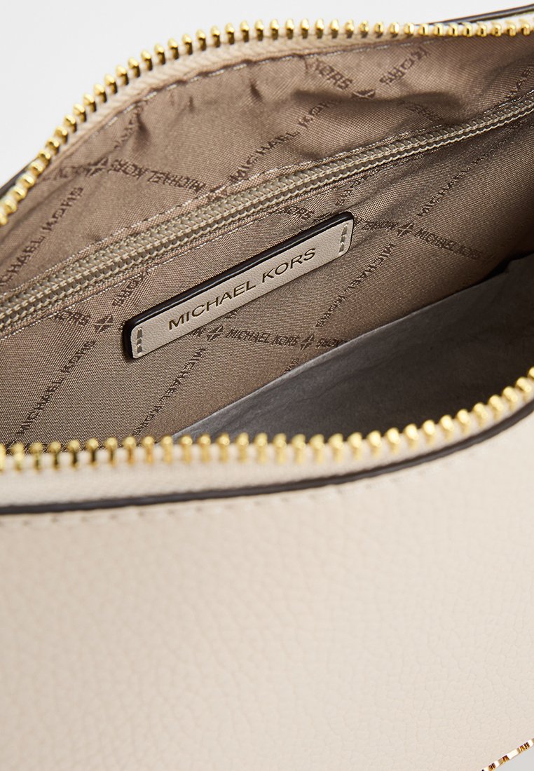Intérieur en cuir beige avec fermeture éclair dorée, présentant une doublure lisse et une étiquette de logo cousue avec "MICHAEL KORS."