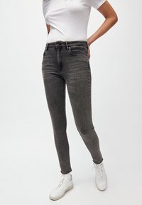 Jeans ajustados grises en tela de mezclilla con un acabado desgastado. Cuenta con un cierre de cremallera y botón, cinco bolsillos y ojales para cinturón.
