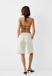 Vita denimshorts med bakfickor, matchade med en svart halterneck-top med tunna band som är knutna i nacken, bärs med svarta klacksandaler.