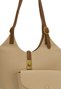 Beige nahkalaukku, jossa on teksturoitu pintakuvio, ruskealla olkahihnalla ja kultaiseen hakasella. Mukana on pieni etutasku napilla.