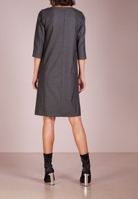 Harmaa, polvenpituinen mekko, jossa on kolmivartiset hihat, suora leikkaus ja takana vetoketju. Yhdistetty mustiin korkeakorkoisiin nilkkabootseihin.