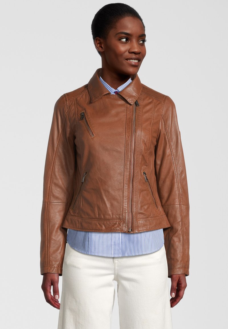 Veste en cuir marron au design ajusté, avec des poches zippées et un col plat, portée sur une chemise rayée bleue et blanche.
