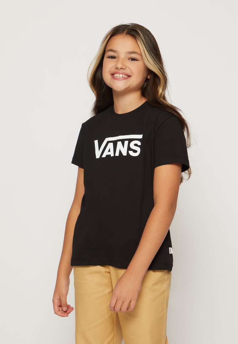Camiseta de algodón negra con el logo blanco de "VANS", mangas cortas, cuello redondo, combinada con pantalones beige. Textura suave, corte relajado.