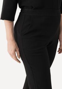 Zwarte op maat gemaakte broek met een comfortabele tailleband, voorzien van zijzakken en een gladde textuur, weergegeven in een semi-profielweergave.