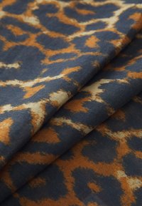 Leopard-patterned fabric in navy, orange, and beige tones, featuring a soft texture and layered folds.