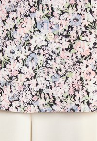 Chemise florale avec un fond noir, ornée de fleurs roses, bleues et vertes. Détail de boutons à l'avant, texture de tissu lisse.