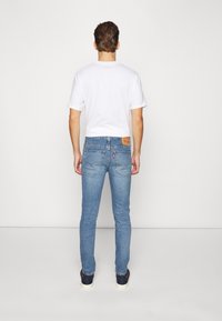 Vaqueros de mezclilla azul claro para hombre con un corte ajustado, que cuentan con un parche de cuero en la cintura y costuras clásicas en los bolsillos traseros.