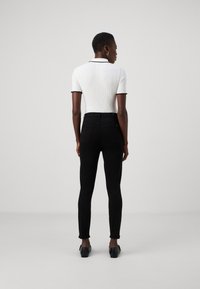 Black skinny jeans with a high waistband, paired with a white ribbed polo shirt featuring black trim on the collar and sleeves.