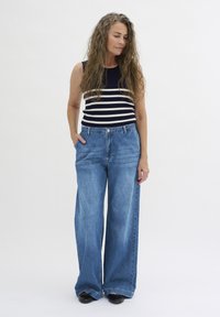 Breda blå jeans i denim, parat med en ärmlös topp i marinblått och vitt randigt mönster. Jeans har hög midja och en avslappnad passform.