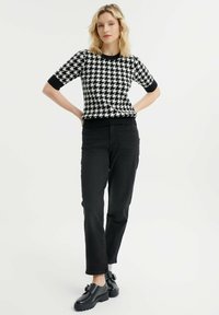 Černobílé svetr s motivem houndstooth a krátkým rukávem, černé žebrované lemy a spodní lem, spárovaný s černými rovnými džíny a robustními černými botami.