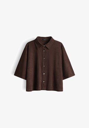 Chemise marron à manches courtes avec boutons, manches larges et col pointu, présentée sur un fond blanc.