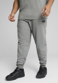 Grå bomulds sweatpants med elastiske manchetter, prydet med et sort Puma-logo på venstre lår og parret med sorte sportssko.