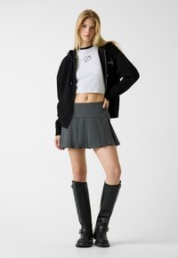 Czarna bluza z kapturem na zamek, szary krótki t-shirt z logo, plisowana szara mini spódnica oraz czarne skórzane kozaki za kolano z klamrami.