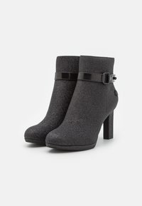 Bottes noires pour cheville avec une finition texturée, dotées d'une bride à boucle noire brillante et d'un talon haut. Aspect lisse avec un bout arrondi.