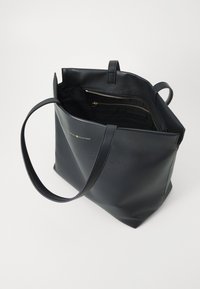 Svart lær toteveske med flat bunn, innvendig lomme med glidelås og gulllogo. Har to lange håndtak for enkel bæring.