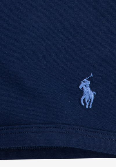 Tamno plava pamučna tkanina s glatkom teksturom, s izvezenim svijetloplavim logom igrača polo na lijevoj strani.