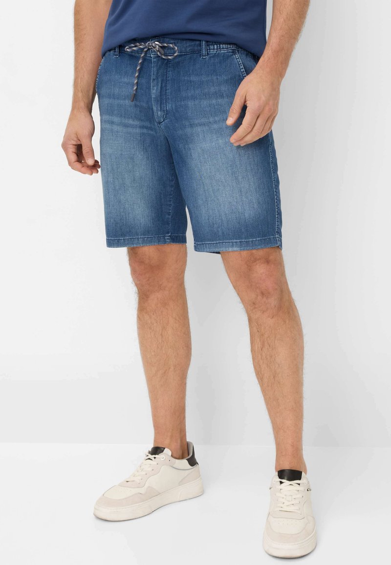 Shorts in denim di un azzurro chiaro con cintura regolabile, caratterizzati da un taglio dritto e orlo che finisce a metà coscia. Indossati con sneakers bianche.